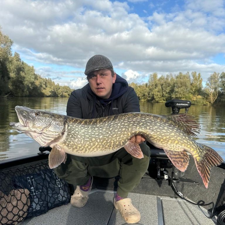 Man in een boot toont een grote snoek met groene en gele schubben.