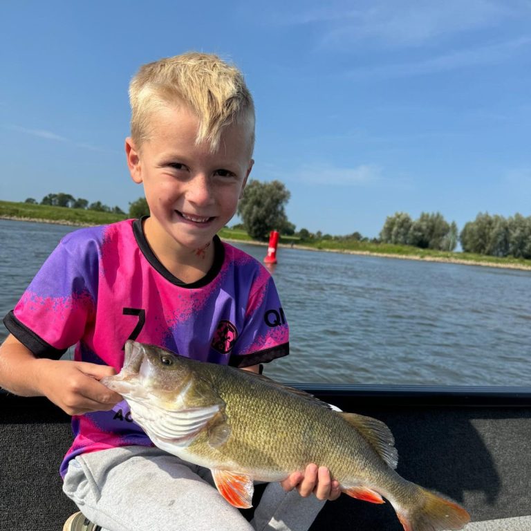 Gelukkige jongen houdt een grote baars vast terwijl hij op het water zit.