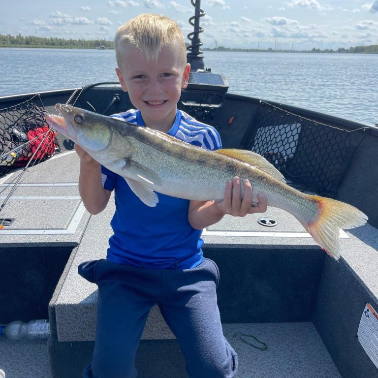Jongen in blauwe shirt houdt een grote vis vast op een boot.