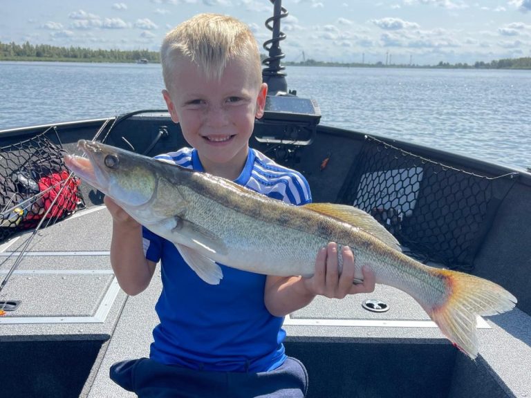 Vissersman houdt een grote snoek vast op een boot in het water onder een blauwe lucht.